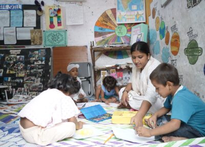 A group of children writing and drawing in a classroom in India sat on the floor with their teacher.