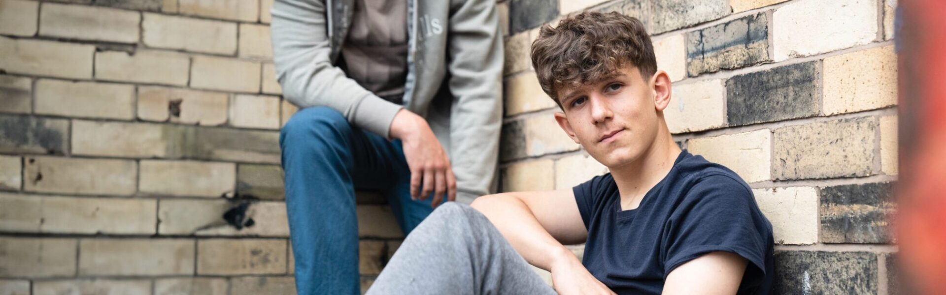 A teenage boy sitting on the floor in front of a wall.