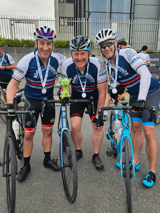 Three men wearing cycling gear and posing on bikes.