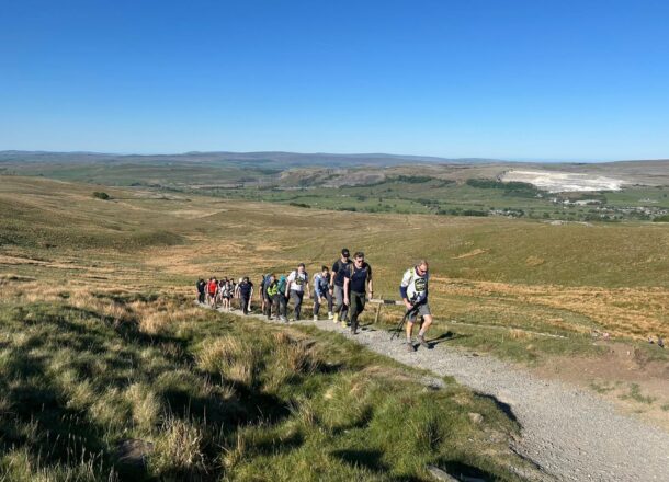 A picturesque view of mountain landscape with a group of hikers taking part in Railway Children's Yorkshire Three Peaks challenge walking uphill.