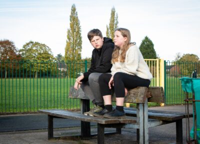 Two teenagers sat on top of a picnic bench at a play area in the UK looking downcast.