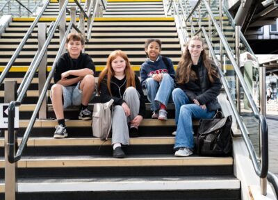 Group of teenagers sat on stairs at a train station.
