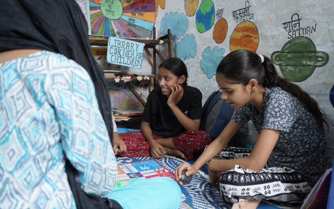 Two girls sat on the floor learning with a Railway Children India project worker at a Child Acitvity Centre.
