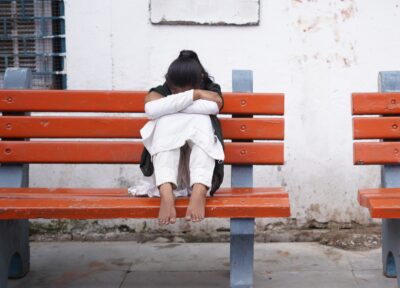 A girl sat on a bench with her legs up, leaning her arms into her legs and her face down.