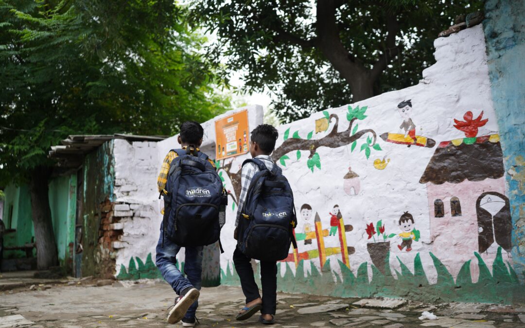 Two young boys carrying Railway Children branded backpacks, walking through their community in India.