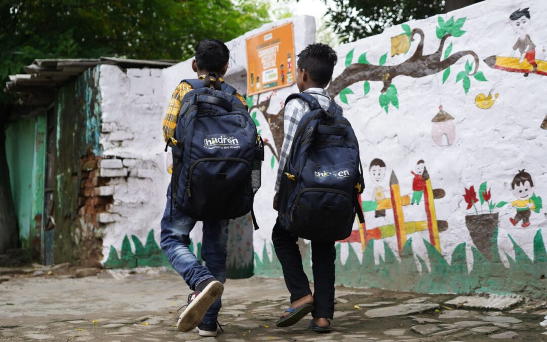 Two young boys carrying Railway Children branded backpacks, walking through their community in India.