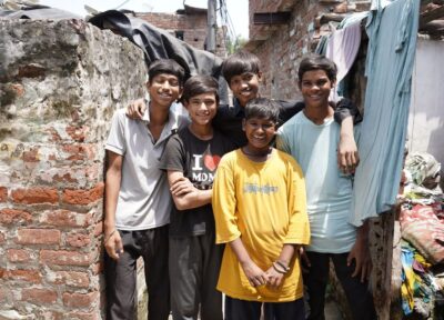 A group of boys on the streets of India in a huddle with their arms round each other and smiling.