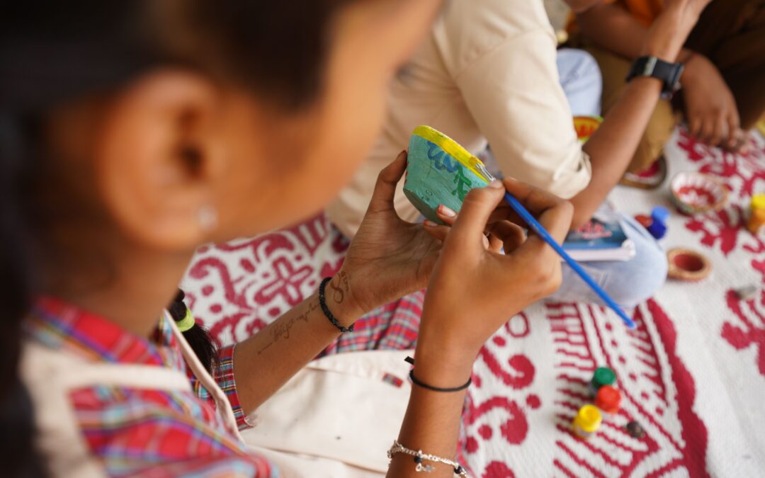 The side profile of a girl who is painting a cup a blue and yellow pattern.