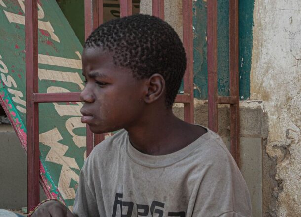 A boy sitting on the streets of Tanzania wearing a grey T-shirt and looking off to the left.