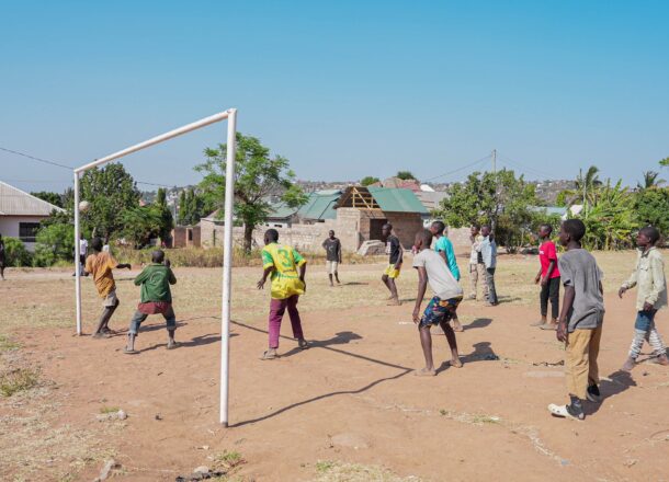 A group of teenagers in Tanzania playing football on some sand with a goal next to them.