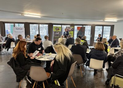 A group of people sat at tables in a function room by a large window.