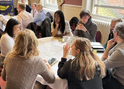 A group of young people and adults having a discussion around a table in a function room.