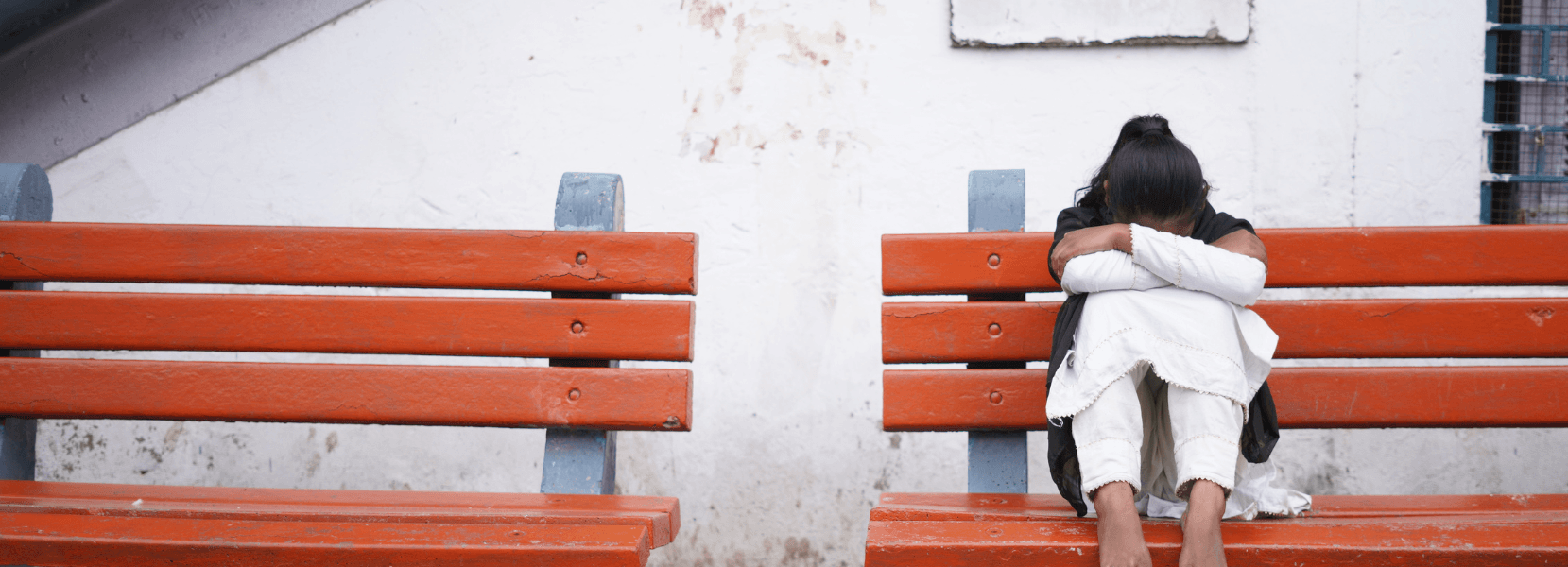 A girl sat on a bench with her legs up, leaning her arms into her legs and her face down.
