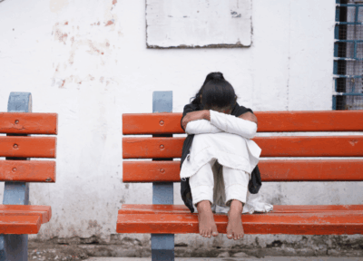 A girl sat on a bench with her legs up, leaning her arms into her legs and her face down.