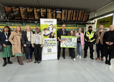 A group of Railway Children staff and rail industry partners stand together at a busy railway station to raise awareness of the charity’s work supporting vulnerable young people. The team are pictured in front of departure boards and ticket barriers, alongside banners promoting Railway Children’s mission to ensure no child is lost to the streets.