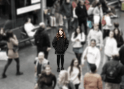 A scene showing a blurred crowd in a railway station around a teenage girl wearing black and looking vulnerable in focus.