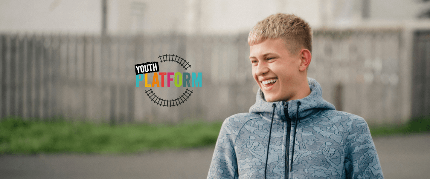 Smiling teenage boy wearing a blue hoodie standing outdoors beside the colourful Youth Platform logo, representing youth voices and empowerment.