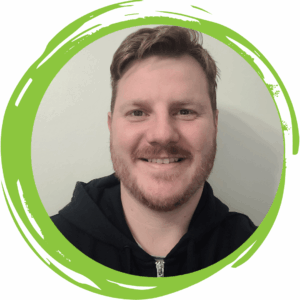 An image of a man with short hair and a moustache smiling at the camera and wearing a black hoodie with a green circle frame surrounding him.