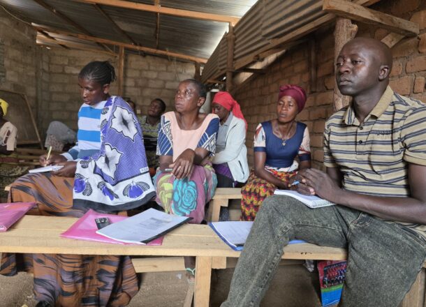 A group of adults sat in a classroom setting in Tanzania with pens and paper taking part in Railway Children Africa's ACT Parenting Programme.