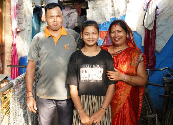 A mother and father stood either side of their teenage daughter, all smiling for the camera in the streets of India.