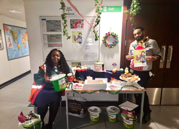 Two fundraisers sat either side of a festive fundraising table with a Railway Children banner and buckets.