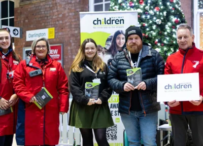 Railway Children and LNER staff stood posing at a station in the UK.