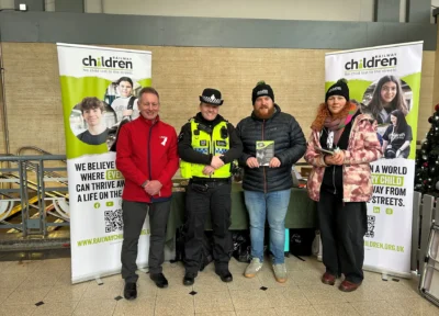 A group of people stood in the middle of two Railway Children banners at a train station in the UK.