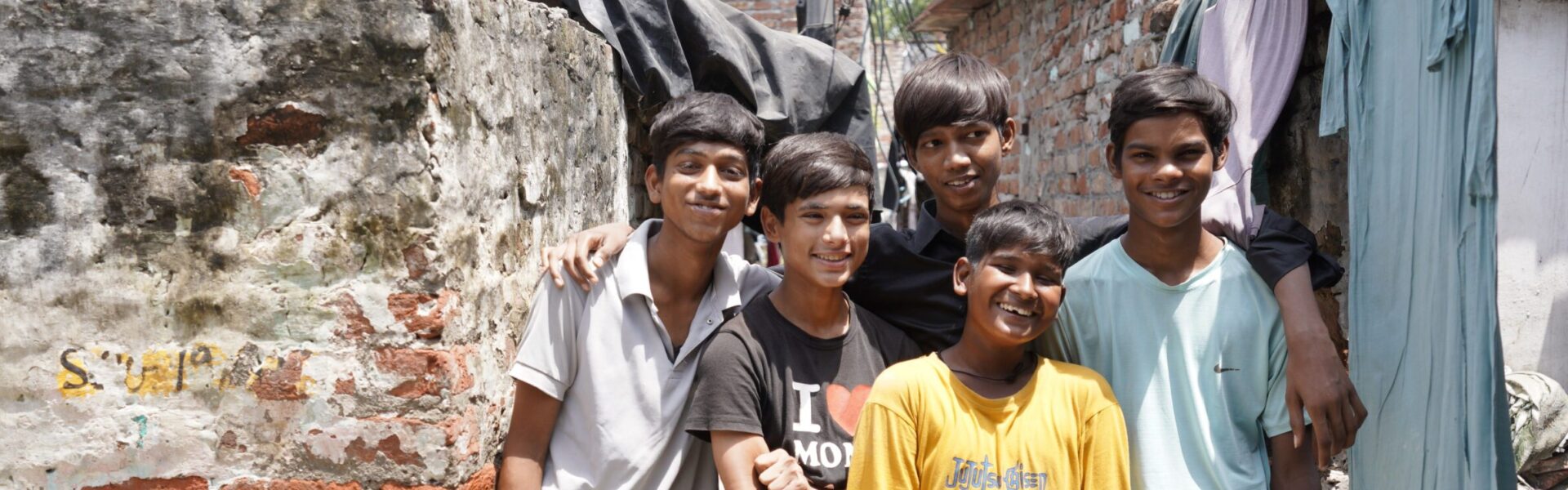 A group of smiling boys standing together in a narrow urban street in India, highlighting community, resilience and hope.