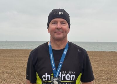 Man wearing a Railway Children events t-shirt, on a beach.