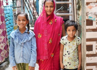 A mother with her two children stood together smiling on the streets of India.