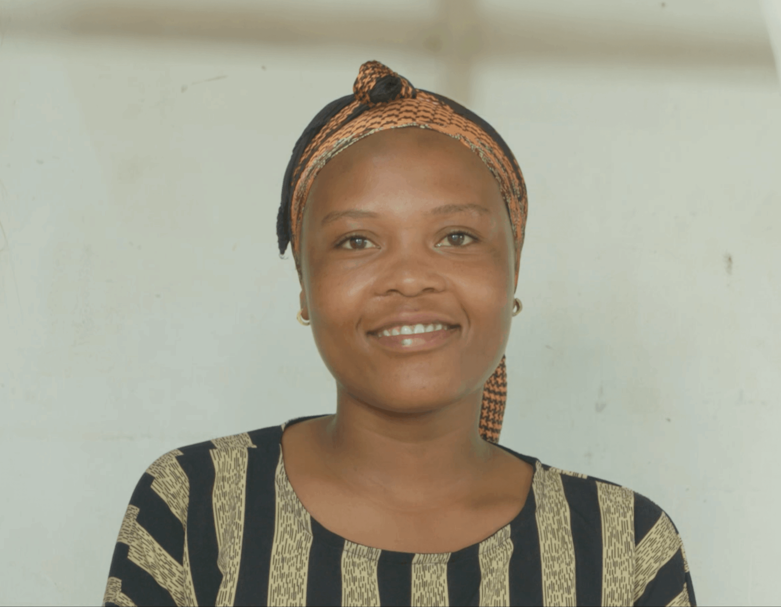 A young woman wearing a patterned top and a headwrap is positioned in front of a neutral indoor background, framed by vertical white cords. She is centred in the image, which highlights Railway Children’s work supporting young people and providing safe spaces.