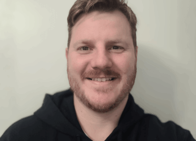 A man wearing a black hoodie taking a selfie and smiling at the camera.