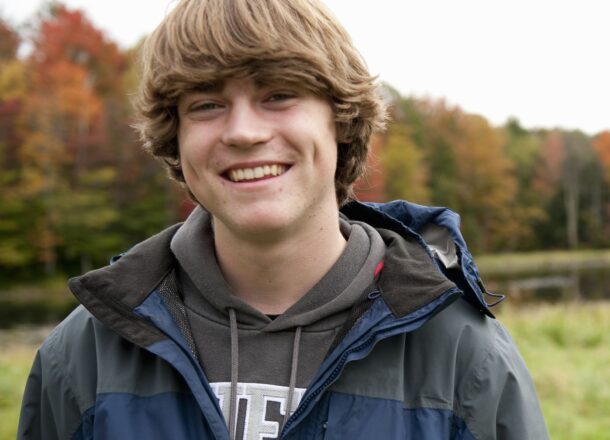 A young person wearing a blue jacket stood in a field in the UK and smiling.