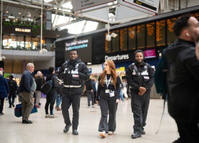 Youth Outreach Worker and South Bank Patrol officers walking through London Waterloo Station near departure boards.