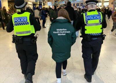 Youth Outreach Worker walking through London Waterloo Station alongside British Transport Police officers during patrol.