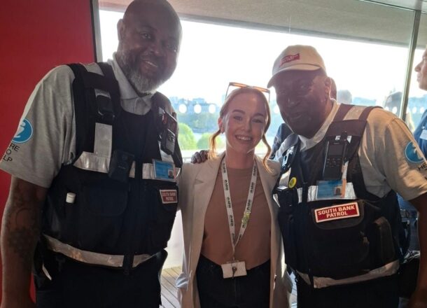 Railway Children staff member standing with South Bank Patrol officers in a station setting, working together to support vulnerable young people.