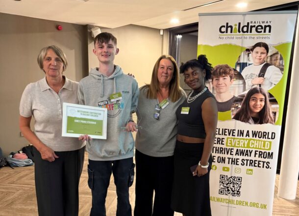 Railway Children youth ambassadors with youth practitioners at an award ceremony next to a Railway Children branded banner.