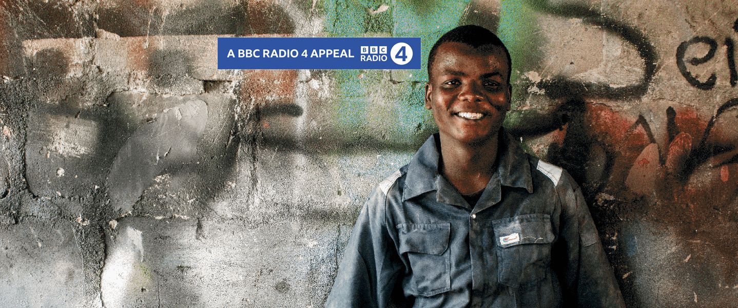 A young adult wearing mechanic uniform leaning against a graffiti wall and smiling with the BBC Radio 4 logo on the image.