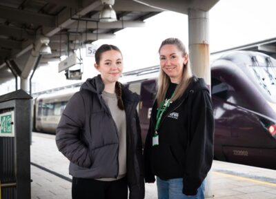 Railway Children youth practitioner with a young person on a railway station platform beside a train, with station infrastructure visible in the background.