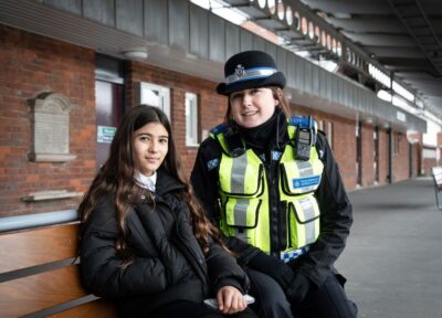 A British Transport Police officer sat on a bench with a young teenager.