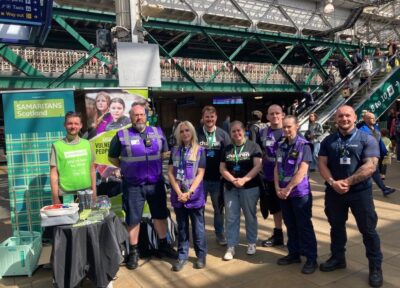 Railway Children, Samaritans Scotland and rail industry partners pose for a group photograph next to rail safety and wellbeing information stands on a station concourse during Rail Safety Week.