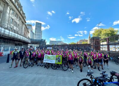 Ride the Route 2026 cyclists celebrate at the finish line with medals, bikes and a Railway Children finish banner after completing the charity cycling challenge.