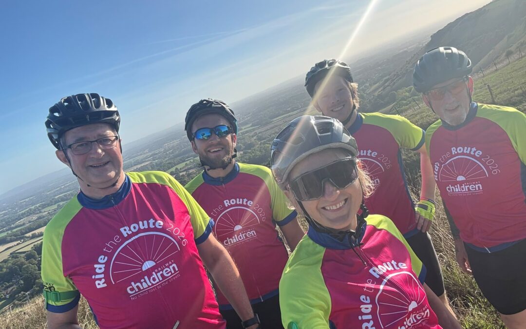 Ride the Route 2026 cyclists pose at a scenic hilltop viewpoint during a Railway Children charity bike ride, with panoramic countryside views in the background.