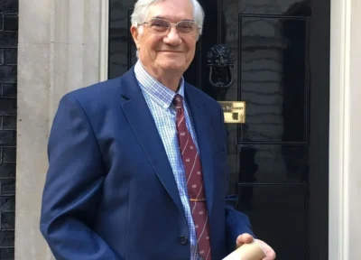 Railway Children founder David Maidment standing outside a government building holding a rolled document.