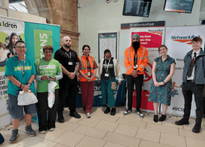 Representatives from Railway Children, Network Rail, the Samaritans, Avanti West Coast and Amulet Security stand together at a station concourse during a Rail Safety Week engagement event, with information banners and safety campaign displays in the background.
