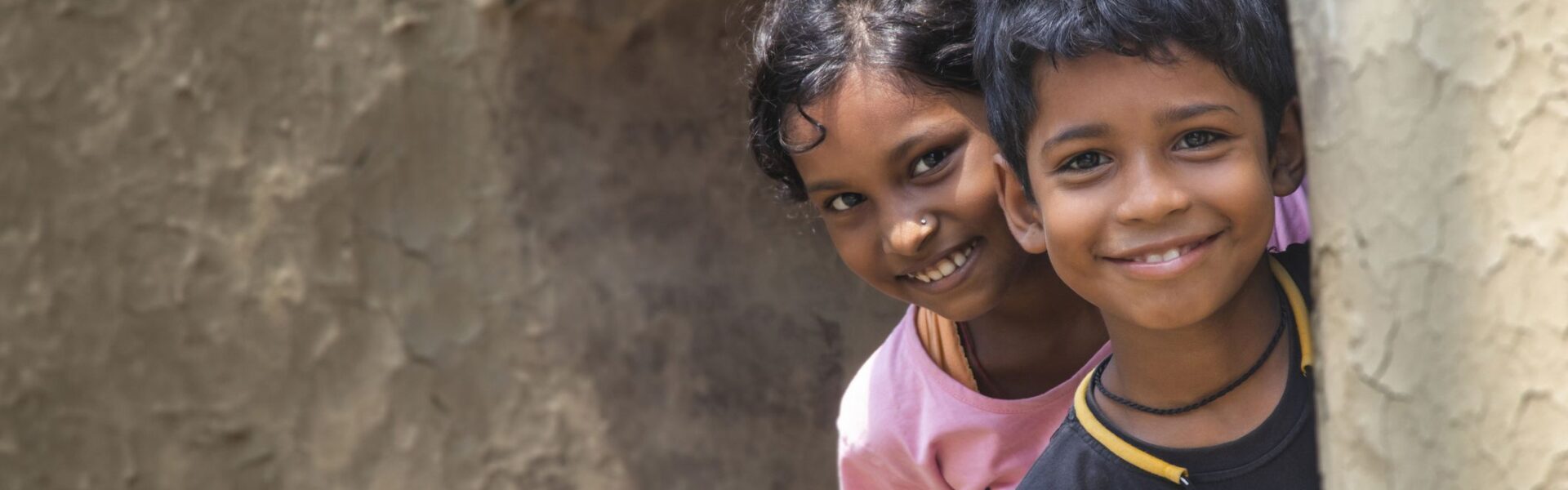 happy boy and girl children peering around a corner