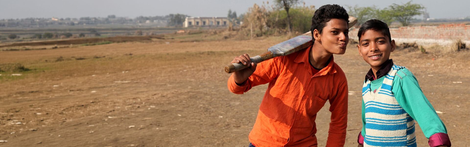 Two children holding cricket bats in an outdoor field, participating in a children's charity sports and development programme.