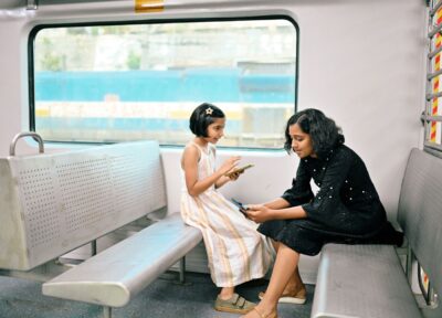 Child and support worker using smartphones while sitting inside a passenger train carriage during a rail journey.