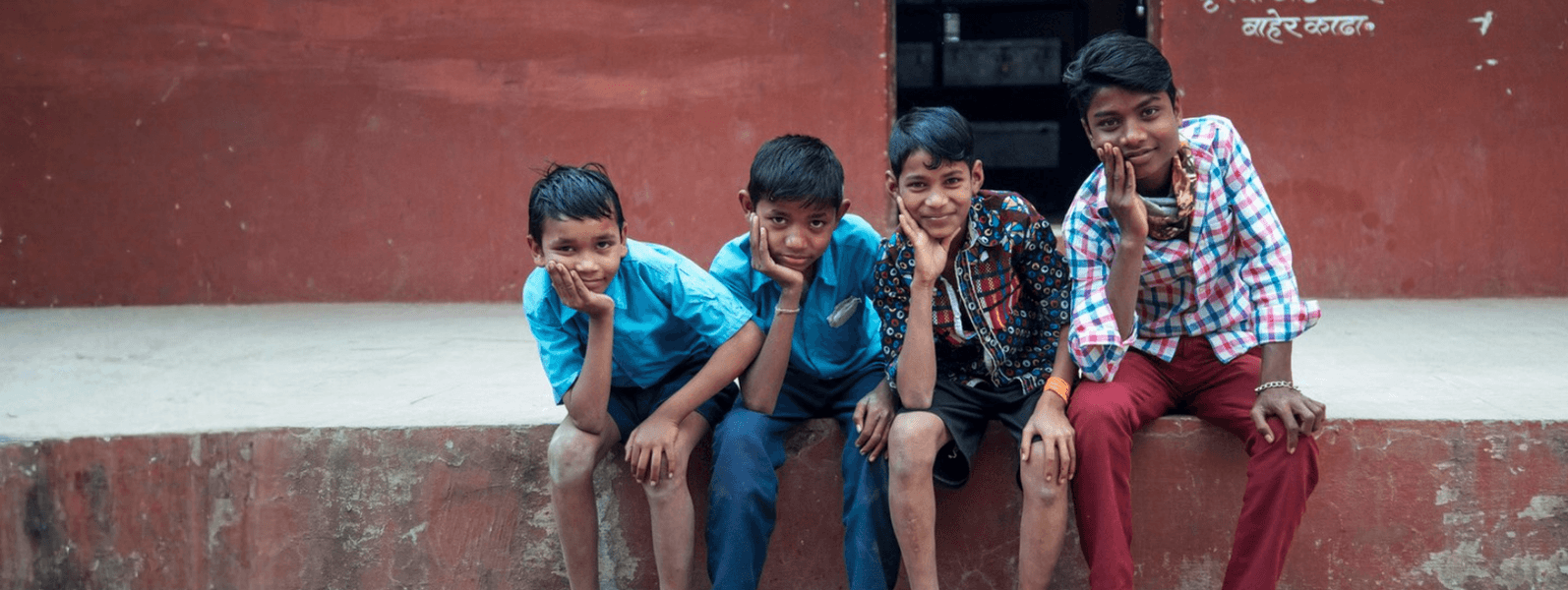 Four young people sitting together outside a red building, looking towards the camera.